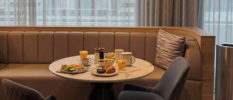 A modern dining area with a round table, two chairs, a sofa, and a breakfast setting.