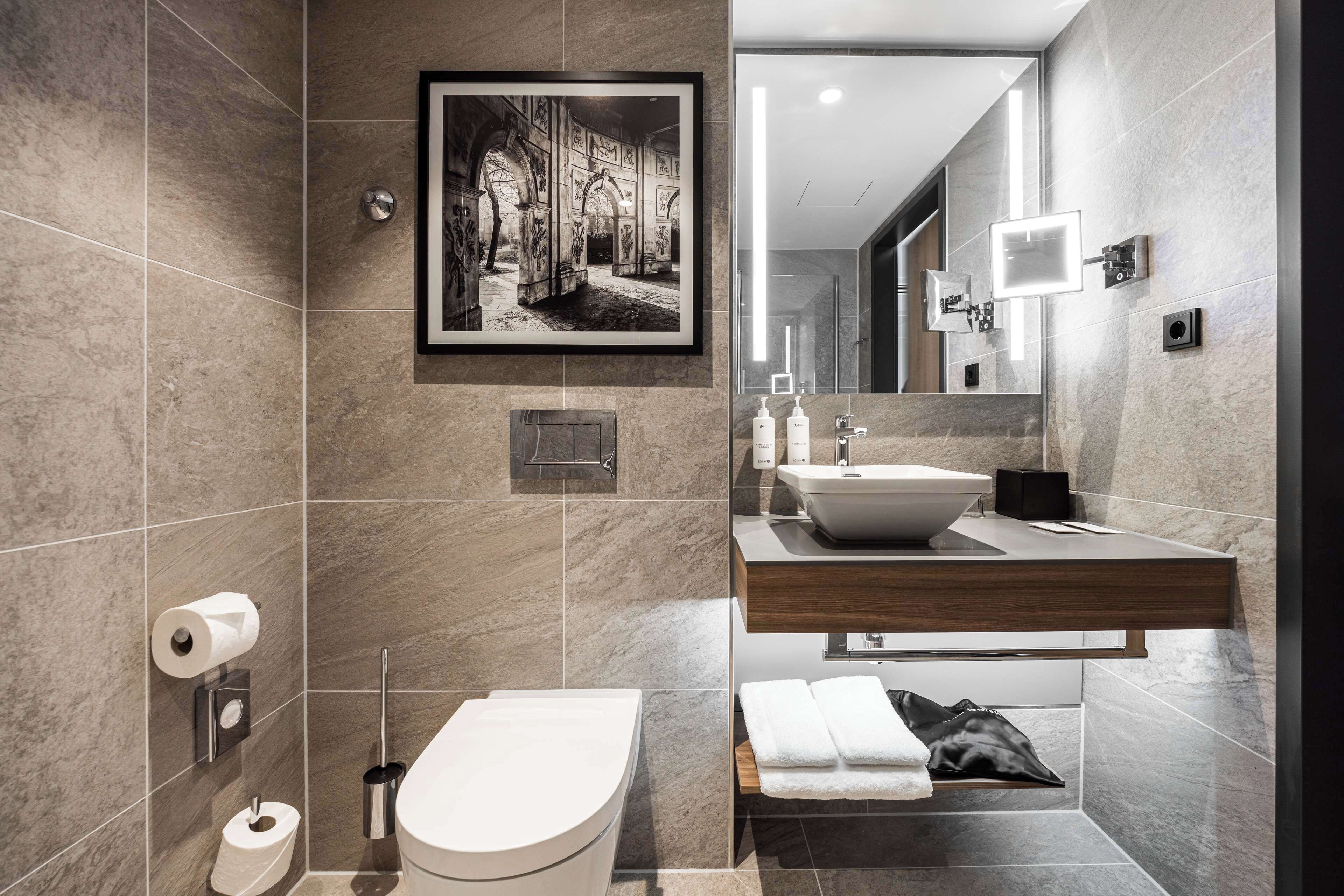 Un baño moderno con suelo de mármol, inodoro, lavabo y un cuadro en la pared.