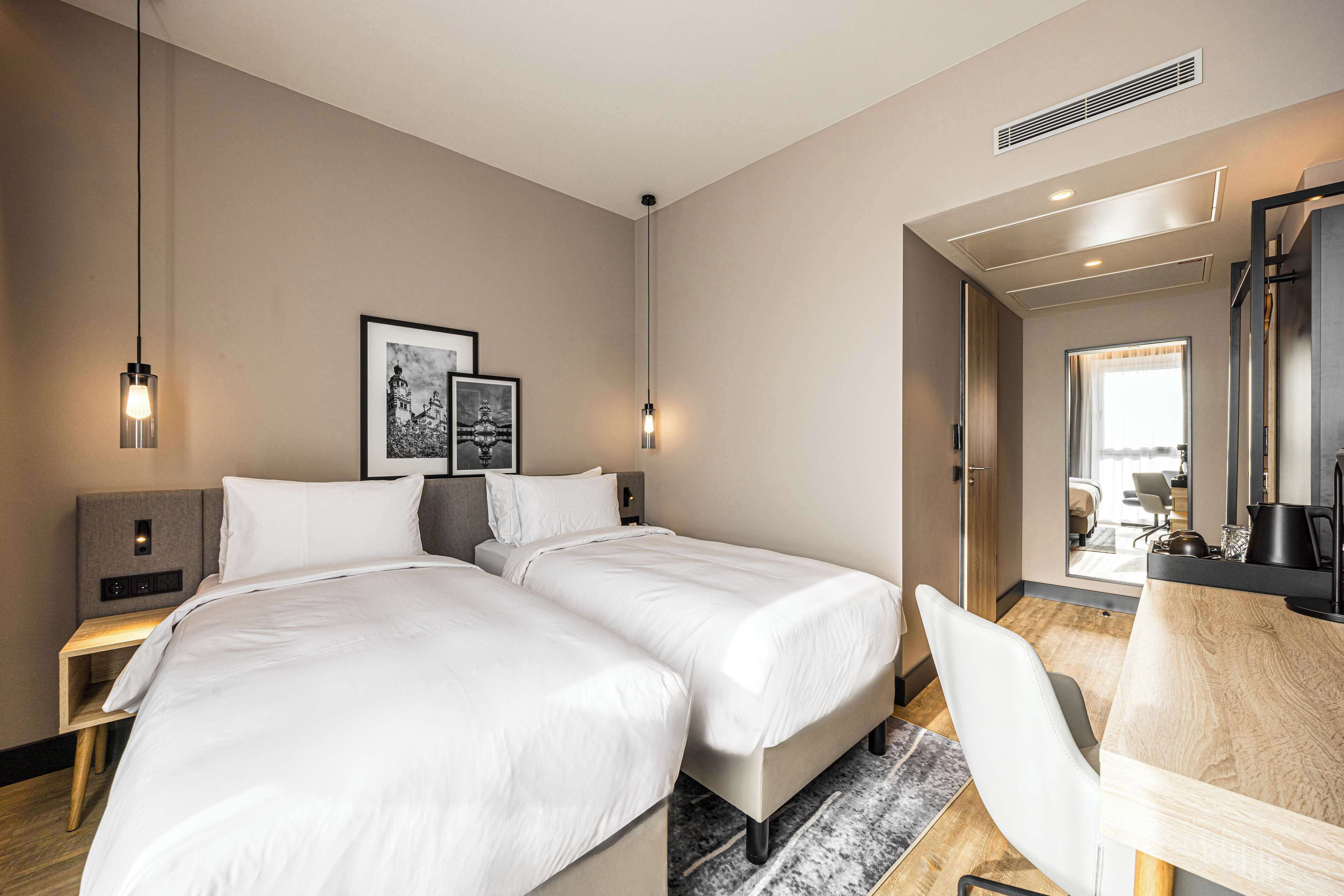 A hotel room with two beds, a desk, a chair, and a large mirror.