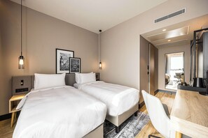 A hotel room with two beds, a desk, a chair, and a large mirror.