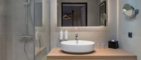 Un baño moderno con cabina de ducha de vidrio, tocador de madera, espejo redondo y lavabo.