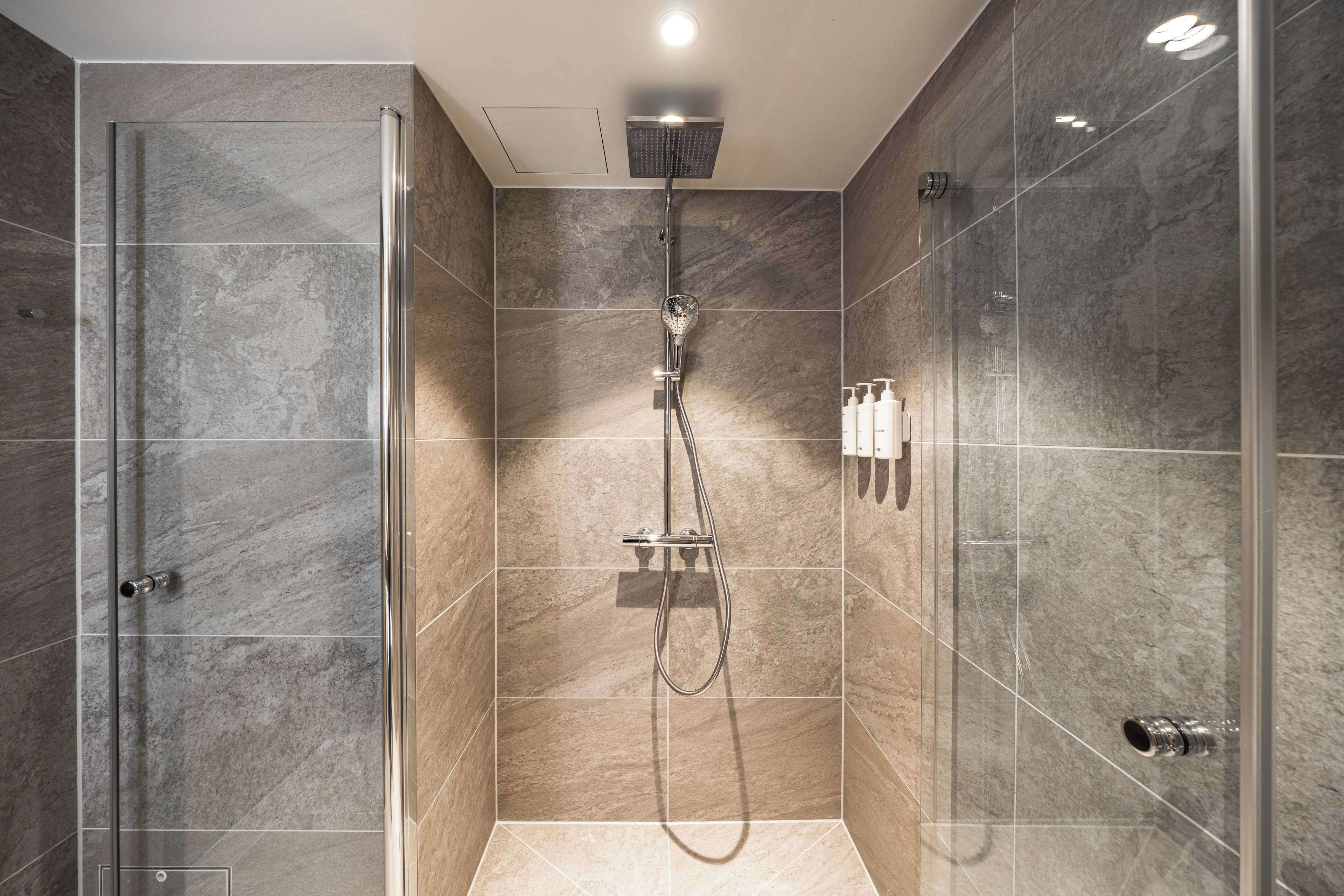 Une douche moderne dotée d’une porte en verre, d’un pommeau de douche à main et d’un robinet mural.