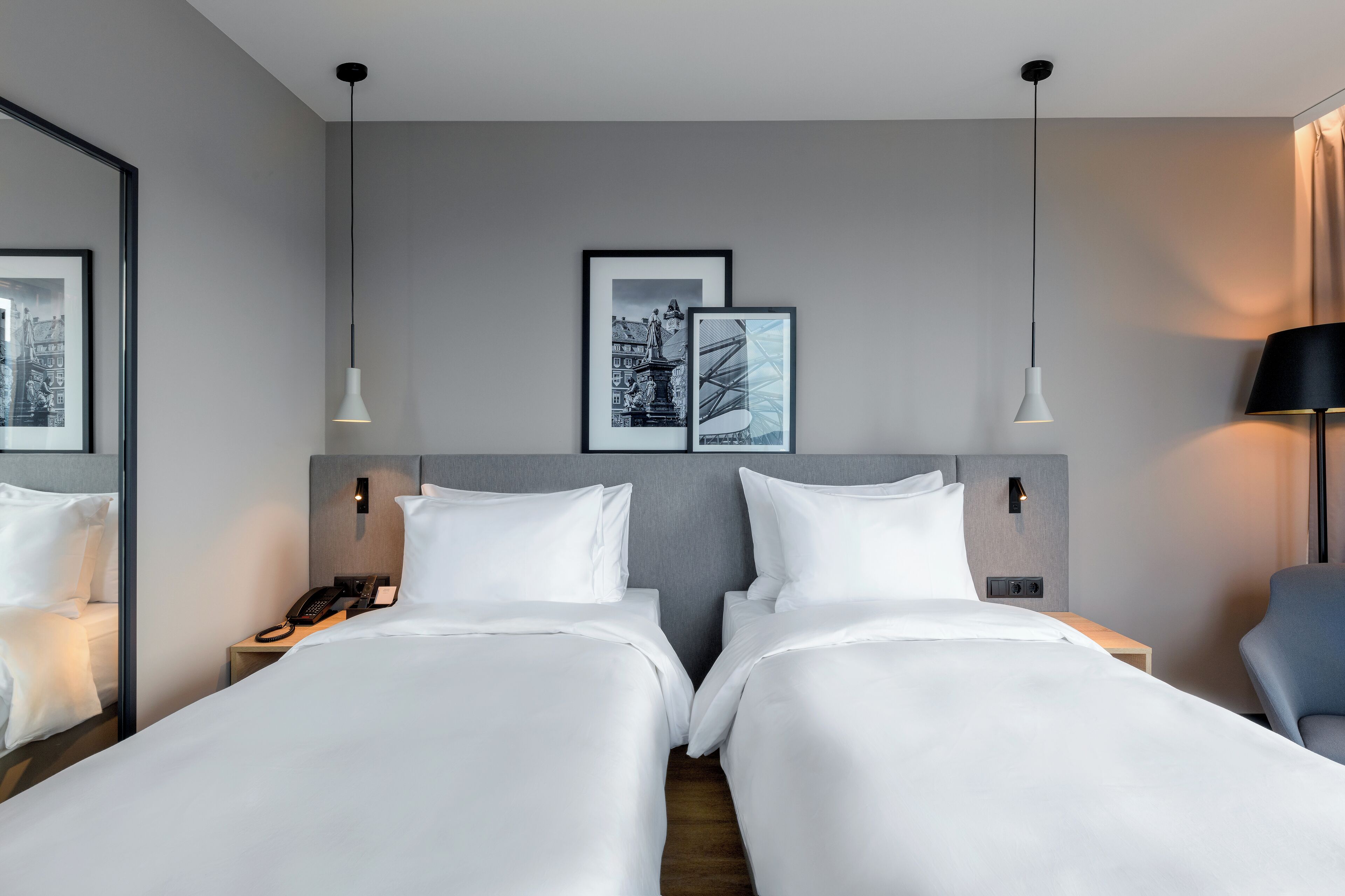 Habitación de hotel con dos camas, una mesita de noche con teléfono, una lámpara y cuadros en la pared.