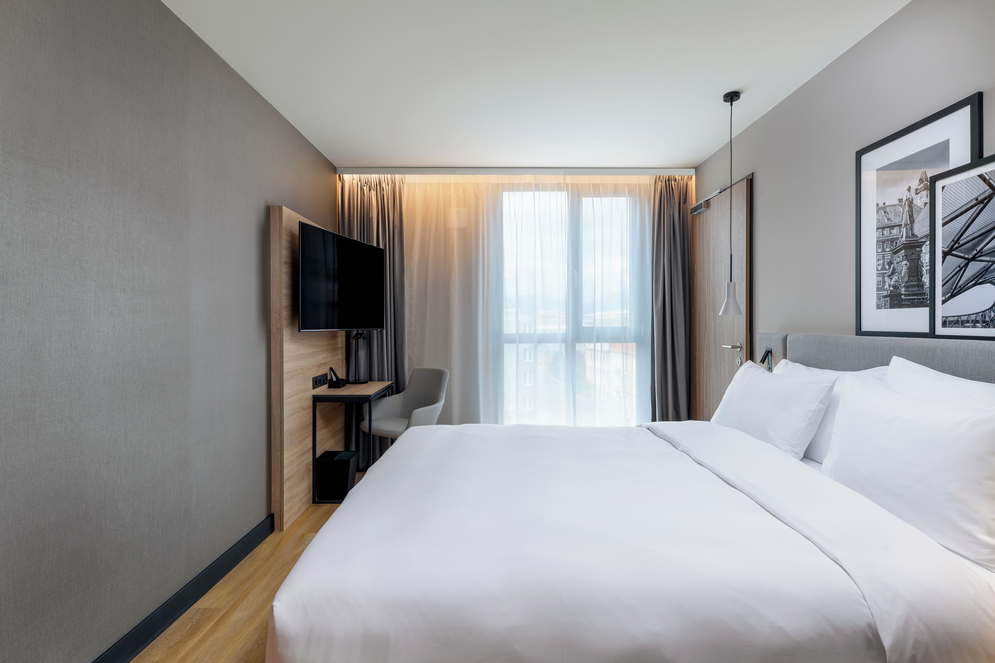 Una habitación de hotel moderna con una cama grande, un televisor de pantalla plana, un escritorio y una ventana con cortinas.