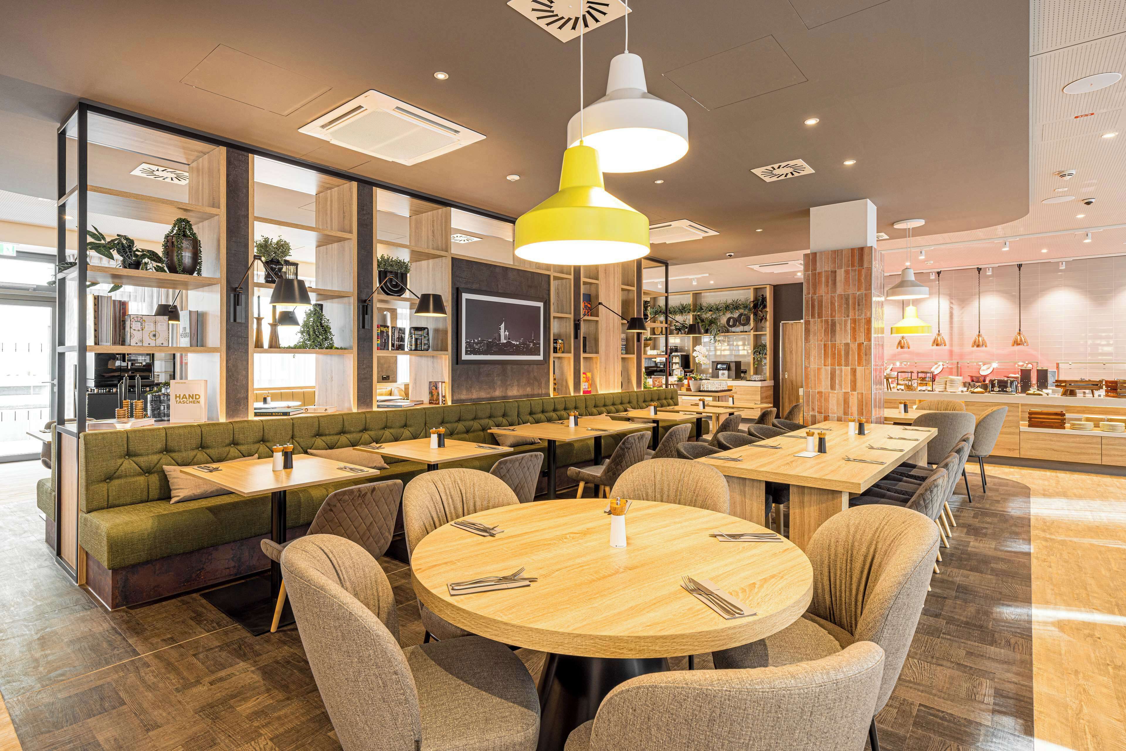 Ein modernes Restaurant mit runden Tischen, gepolsterten Sitzecken und Pendelleuchten.