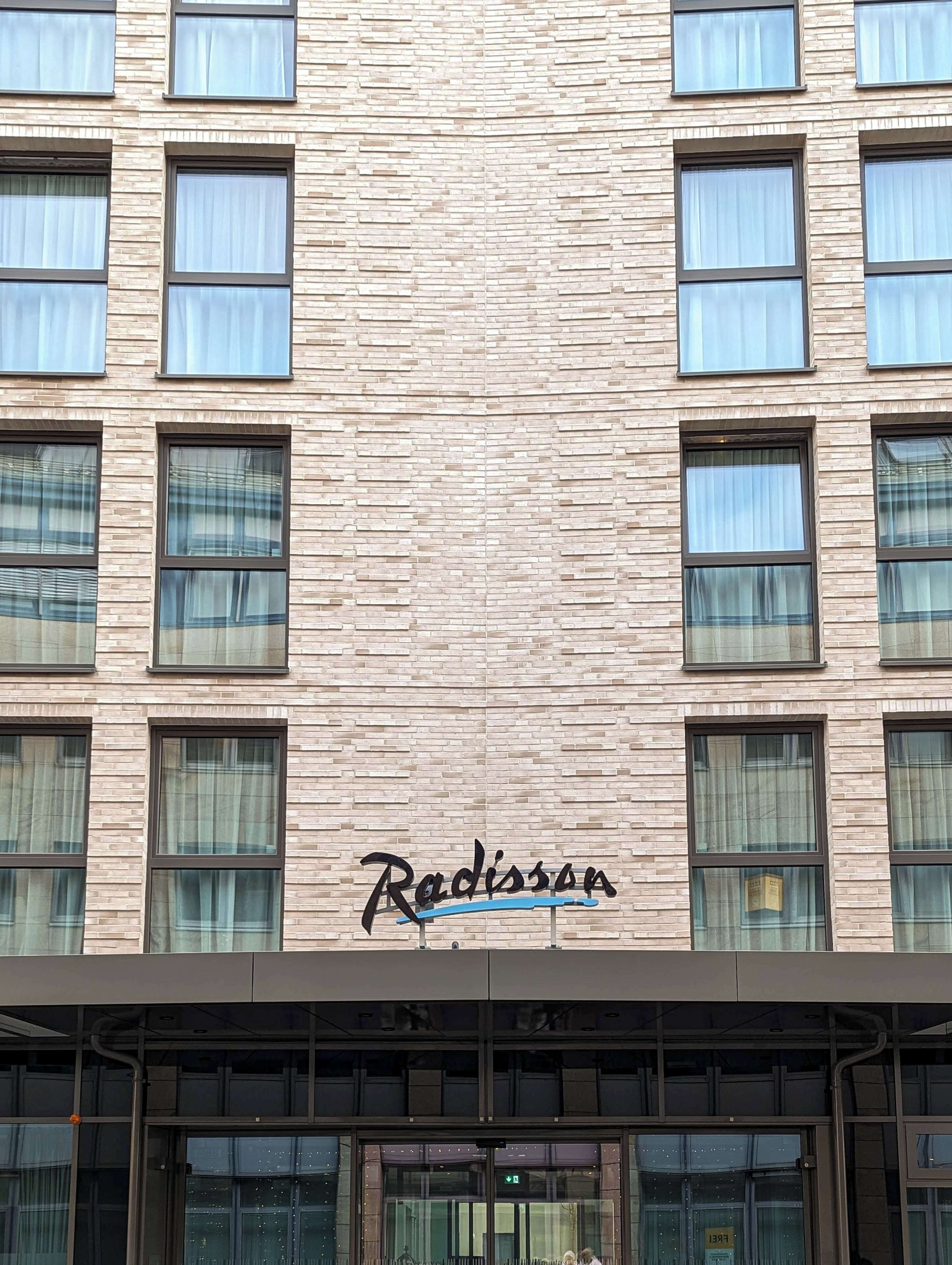 Une façade d’immeuble avec un motif en briques et de nombreuses fenêtres. Le nom « Radisson » est affiché en évidence sur le bâtiment.