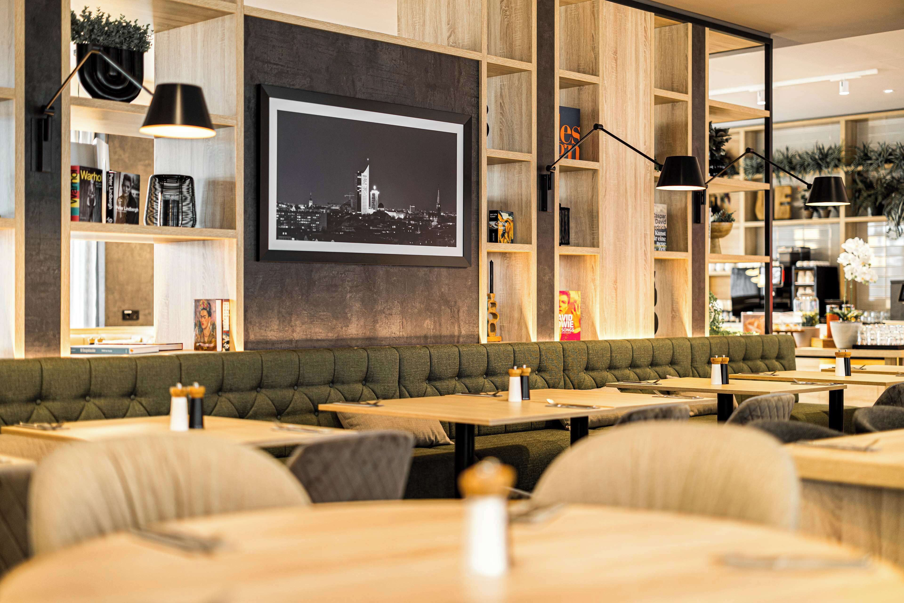 A modern restaurant with a green cushioned booth seating area, wooden tables, and black pendant lighting.