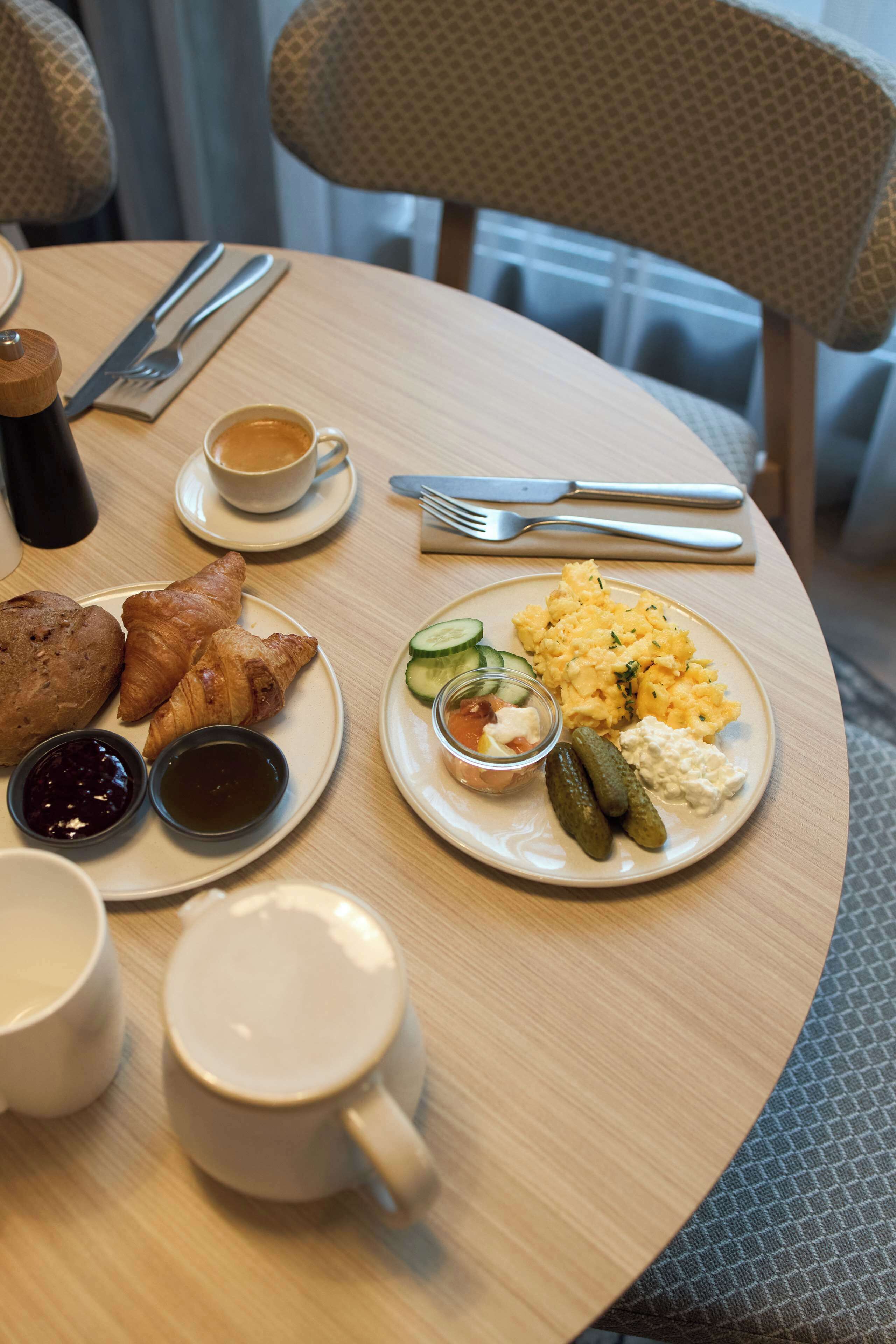 A breakfast setting with croissants, scrambled eggs, and a cup of coffee on a round table.