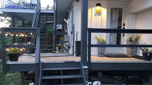 Un espacio al aire libre cubierto con una escalera de madera que sube a una terraza, rodeado de plantas en macetas e iluminación exterior.