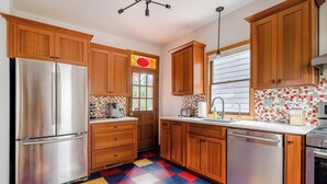 A kitchen with wooden cabinets, a stainless steel refrigerator, a dishwasher, and a colorful checkered floor.