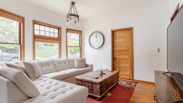 A living room with a sectional sofa, a wooden coffee table, a clock on the wall, and a TV stand.