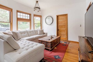 Een woonkamer met een hoekbank, een houten salontafel, een klok aan de muur en een tv-meubel.
