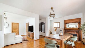 A spacious living room with a wooden dining table, two chairs, a sofa, a TV, and a fireplace.