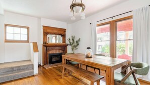 A wooden dining table with benches, a fireplace, and a large window with curtains.