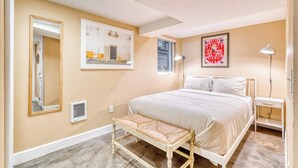 A bedroom with a bed, a bench, a bedside table, a mirror, and two wall-mounted lamps. - Private Underground Getaway - 92 WalkScore (Portland)