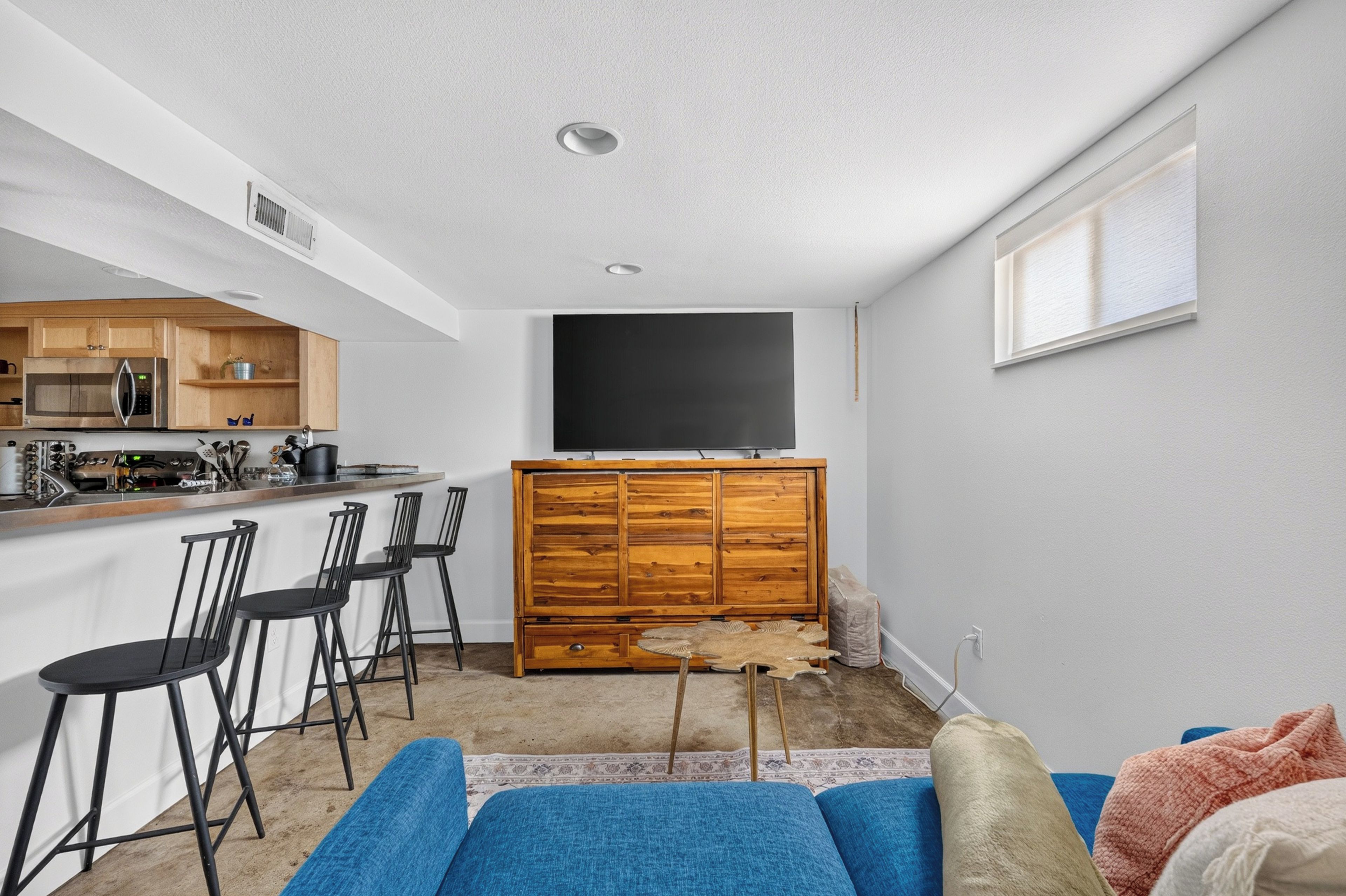 A compact living space with a kitchenette, a dining area with bar stools, and a seating area with a sofa and cushions.