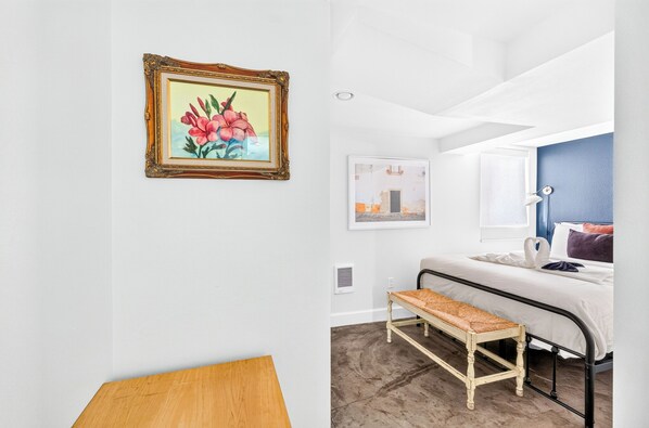 A bedroom with a bed, a bench, a picture frame, and a wall-mounted light fixture.