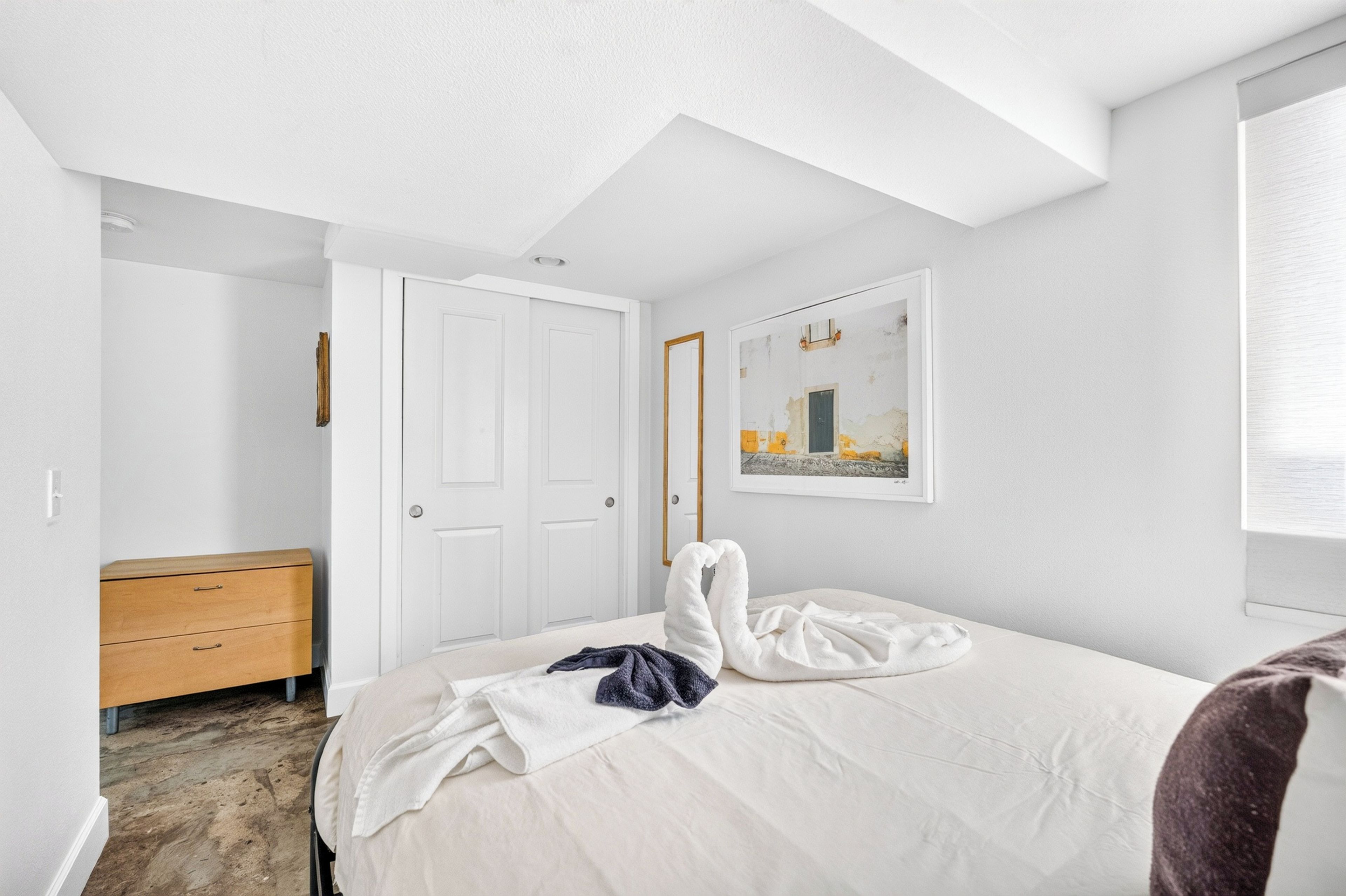 A bedroom with a bed, a wooden dresser, a door, and a framed picture on the wall.