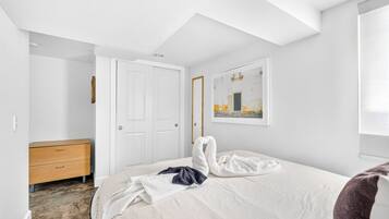 A bedroom with a bed, a wooden dresser, a door, and a framed picture on the wall.