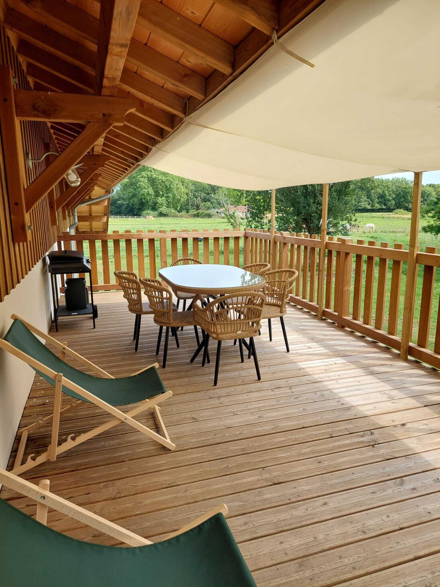 Eine überdachte Terrasse mit Holztisch und -stühlen, einem Grill und einem Liegestuhl.