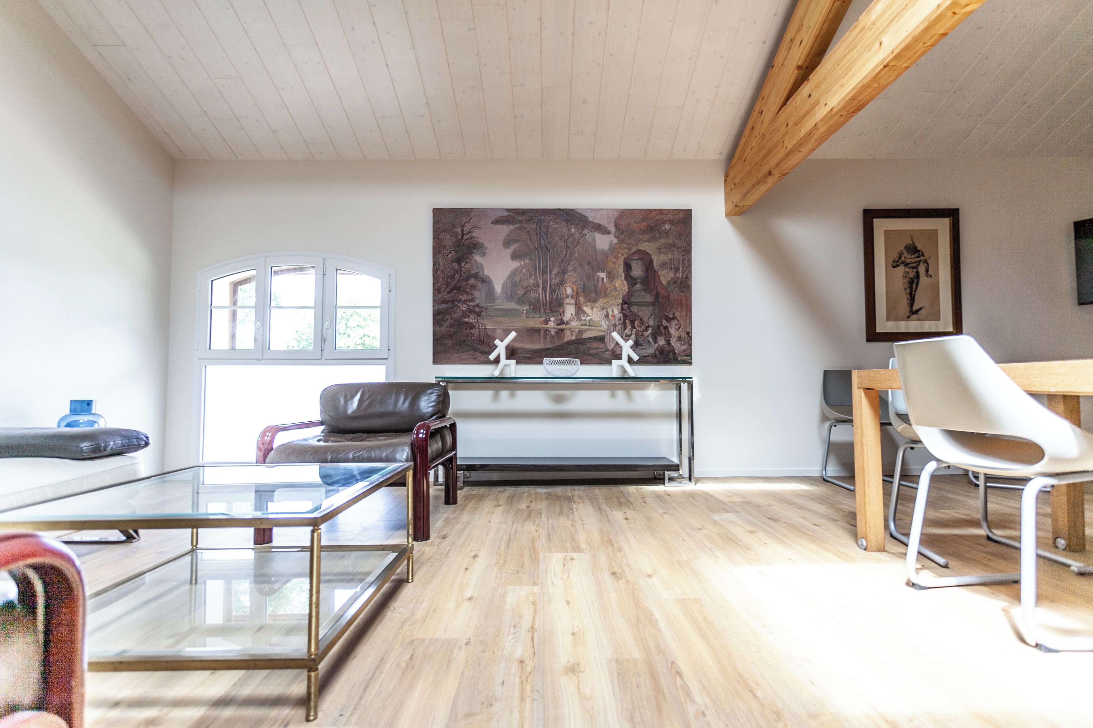 A modern living room with a glass coffee table, leather sofa, and a dining area with a wooden table and chairs.
