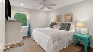 Un dormitorio con cama, ventilador de techo, ventana con cortinas y una obra de arte en la pared.