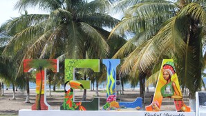 Una escultura colorida con motivos tropicales y el texto "Ciudad Desirable" en una playa con palmeras.