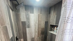 A shower area with a tiled floor, a showerhead, and a curtain. - The Cabin at the lodge (Sodus Point)
