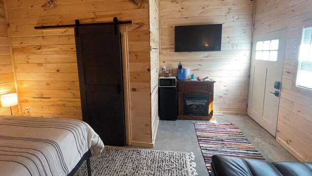 A wooden cabin room with a bed, a TV mounted on the wall, a fireplace, and a sliding door. - The Cabin at the lodge (Sodus Point)