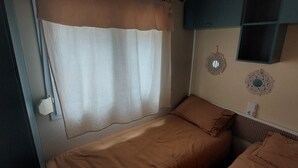 A small, cozy room with a bed, a curtain, and decorative wall hangings. - Spatieux Mobile Home DE 40m2 + Terrasse (Hyères)
