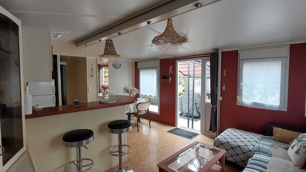 A modern living room with a sofa, a coffee table, and two bar stools. There is a dining area with a table and chairs, and a kitchen area with a refrigerator and a microwave. - Spatieux Mobile Home DE 40m2 + Terrasse (Hyères)