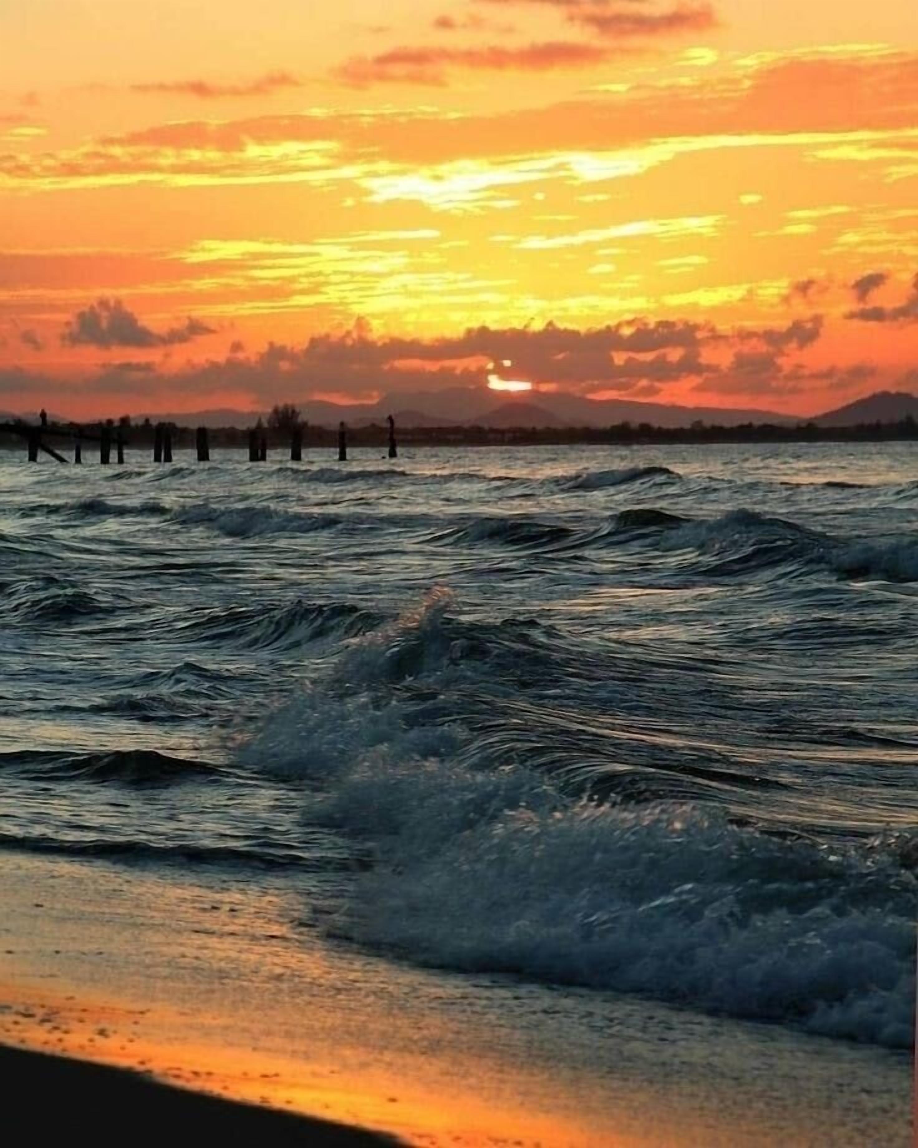 A sunset over a body of water with waves and a distant shoreline.