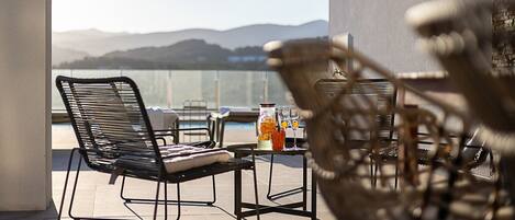 A balcony with a view of mountains, a table with drinks, and two chairs.