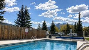 A swimming pool with a wooden fence and a warning sign, surrounded by trees and mountains. - Quaint Riverside Cabin # 1 (Crowsnest Pass)