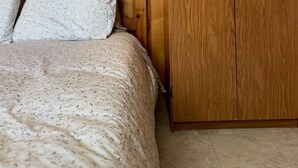 Une chambre à coucher avec une armoire en bois, un lit recouvert d’une couvre-lit à motifs floraux et une tête de lit en bois.