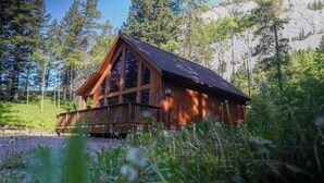 A wooden cabin with a balcony, surrounded by trees and a rocky hillside. - Crowsnest River Chalet - Yeti (Crowsnest Pass)
