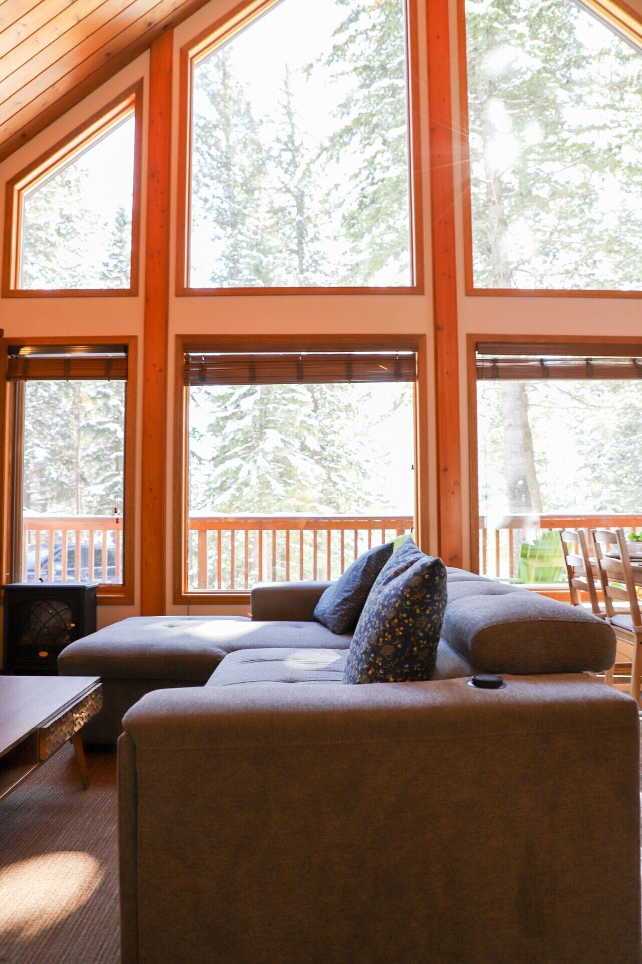 A cozy living room with a sectional sofa, large windows, and a wooden deck.