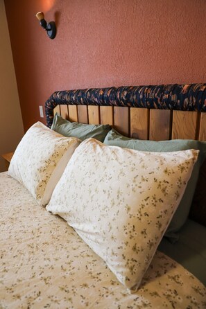 Ein Bett mit blumigem Bettzeug und Kissen, ein hölzernes Kopfende und eine Wandleuchte.