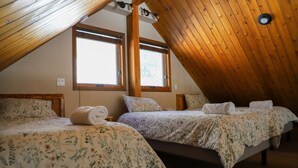 A bedroom with two beds, wooden ceiling beams, and large windows. - Crowsnest River Chalet - Yeti (Crowsnest Pass)