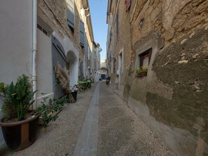 Une ruelle étroite, bordée de bâtiments des deux côtés, dont certains sont dotés de balcons et de plantes en pot.