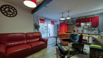 A living room with a red leather sofa, a black leather chair, and a red curtain. There is a kitchen area with red cabinets and a sign that says "NEW YORK".