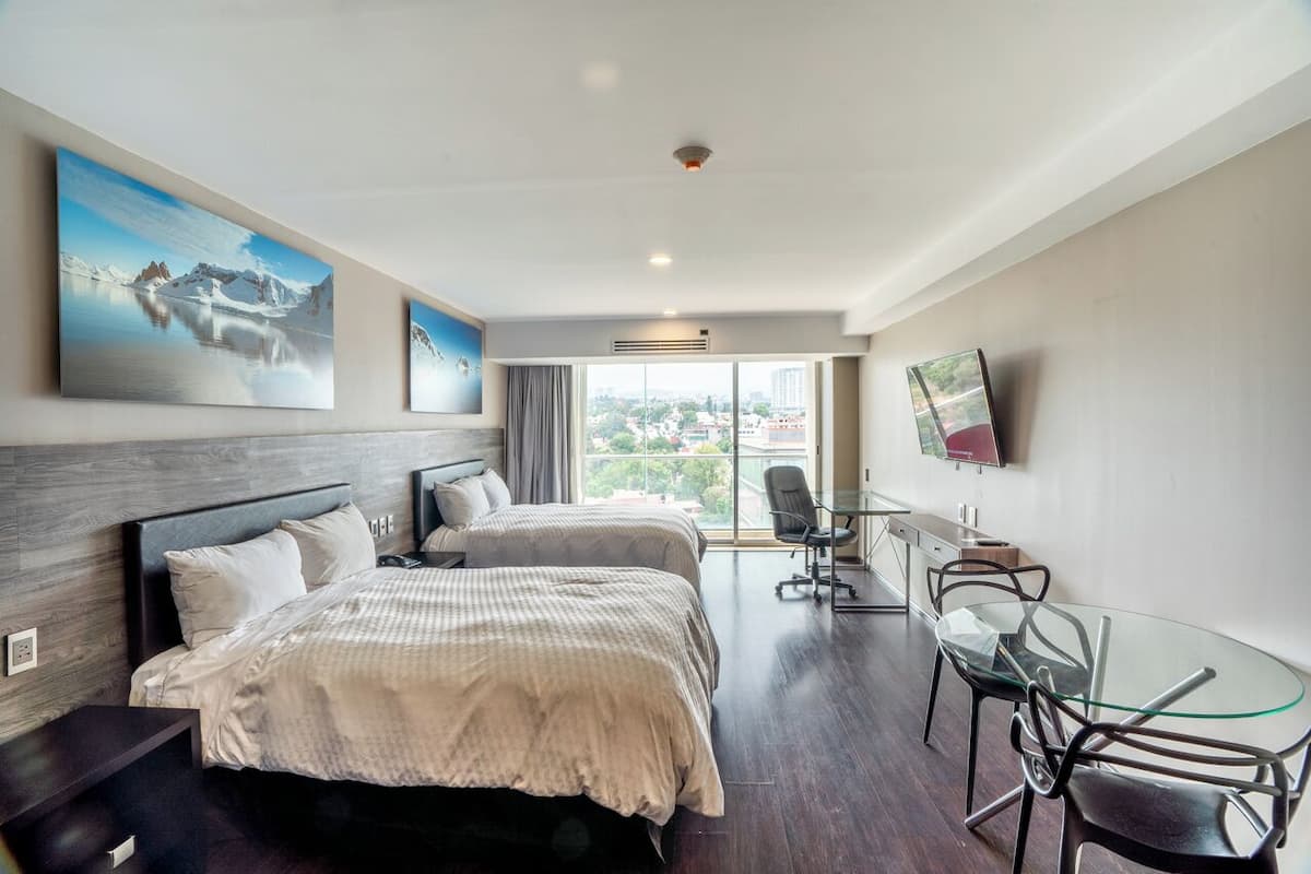 Quarto de hotel moderno com duas camas, uma mesa de jantar de vidro e vista para a cidade.