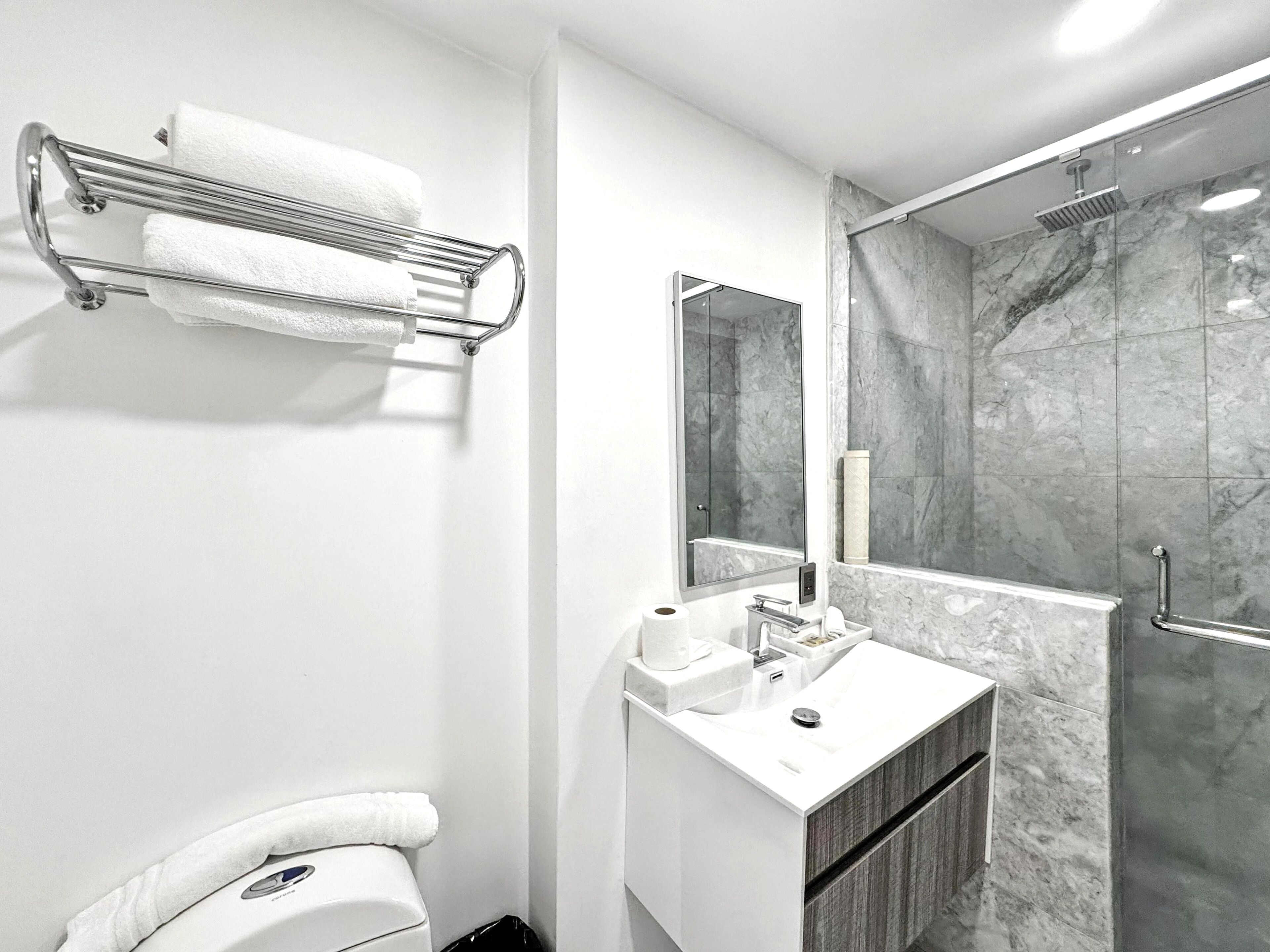 A modern bathroom with a marble shower, a white sink, and a towel rack.