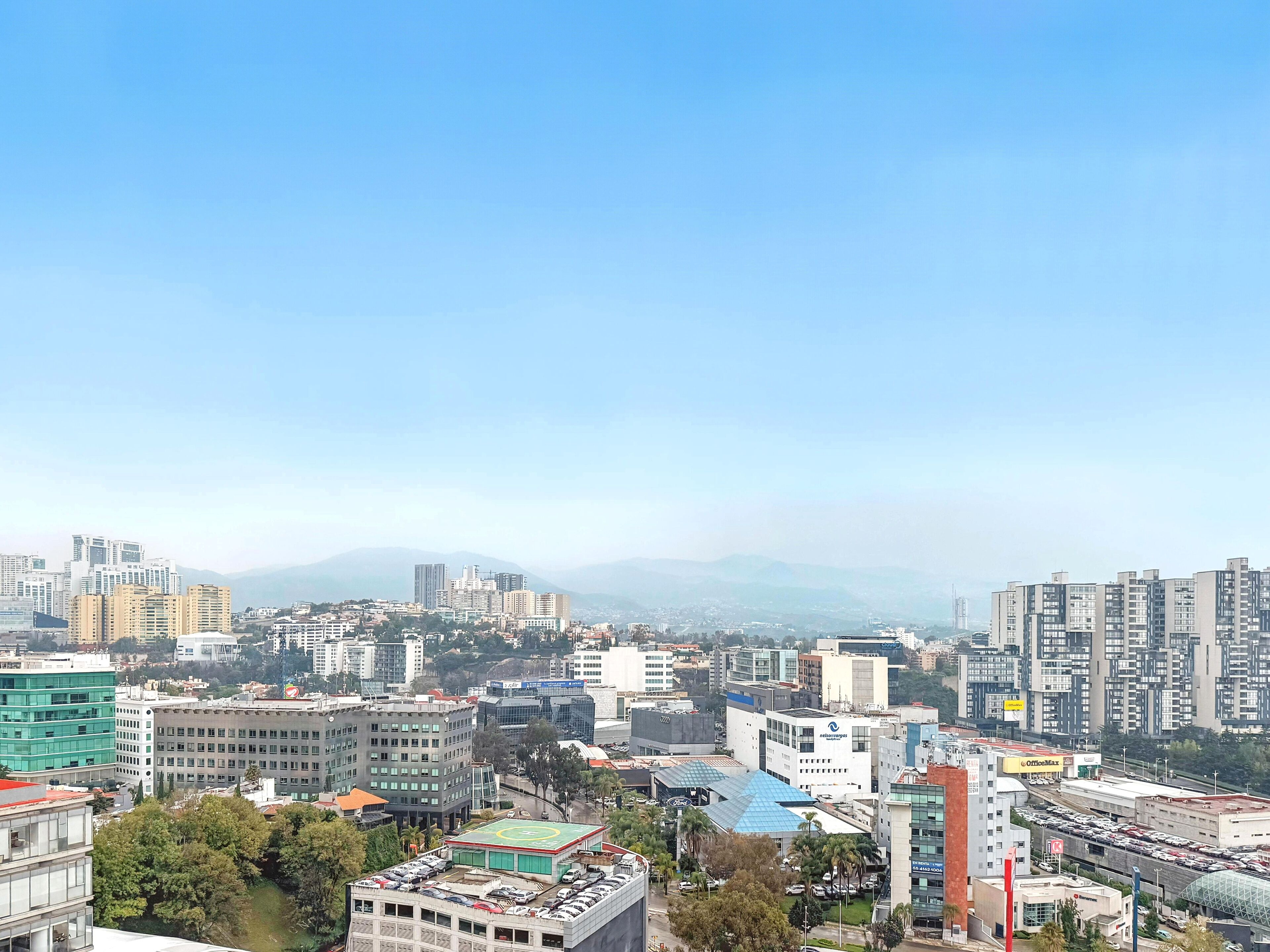A cityscape with high-rise buildings, a sports field, and a parking lot.