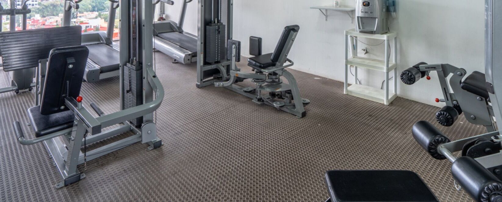 A gym with treadmills, weight machines, and a bench.