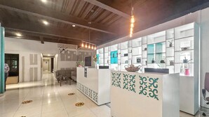 A modern reception area with a white reception desk, tiled floor, and a ceiling with exposed beams. - Elite 47 Unity (Huixquilucan)