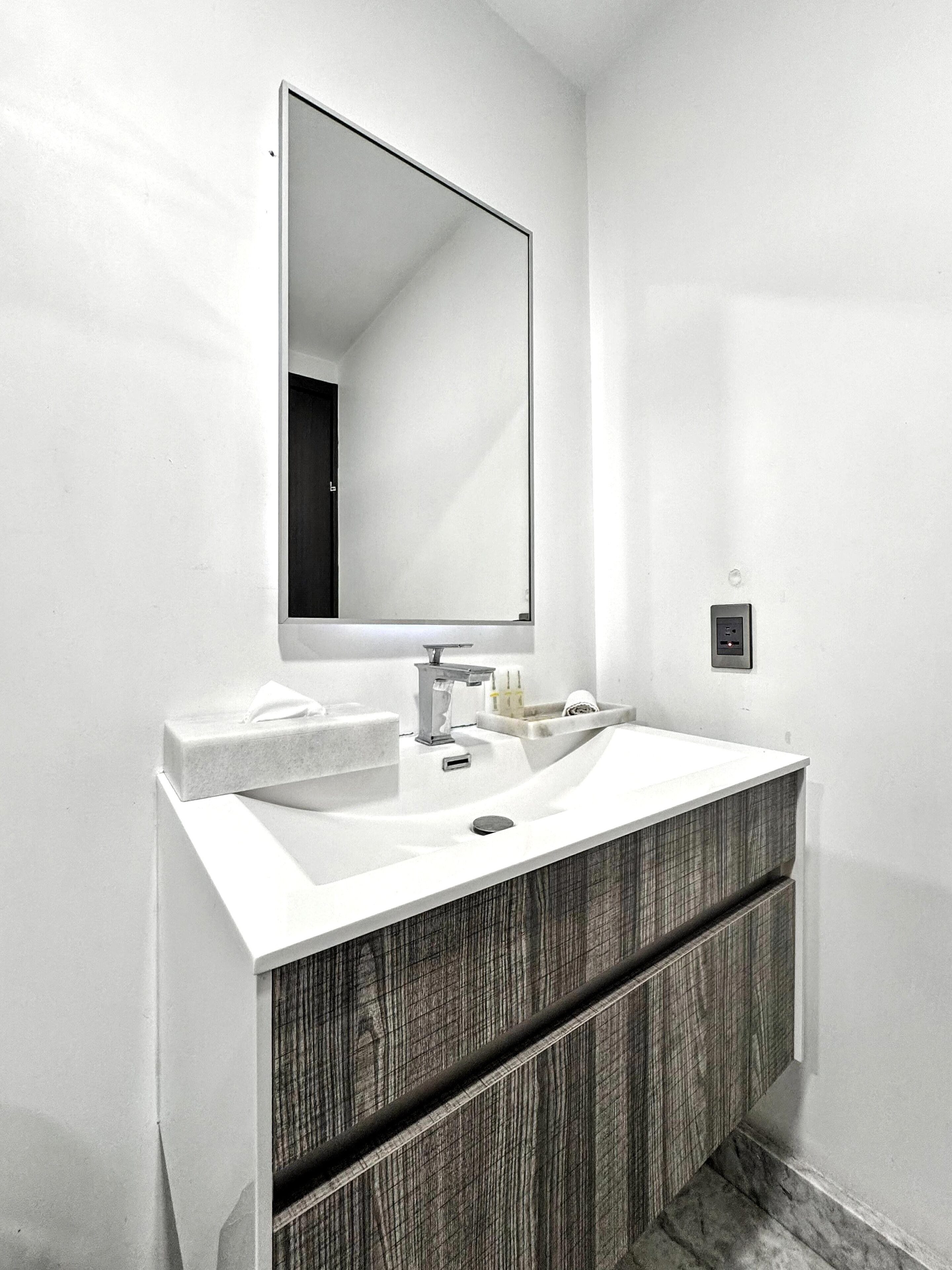A modern bathroom with a white sink, a large mirror, and a wooden vanity.