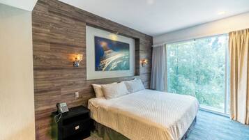A modern hotel room with a large bed, a painting of the Eiffel Tower, a nightstand with a phone, and a window with curtains.