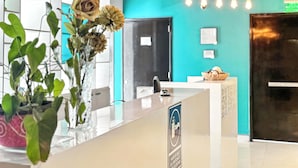 A reception desk with a vase of flowers, a teal wall, and a sign indicating a hand sanitizer station. - Elite 47 Unity (Huixquilucan)