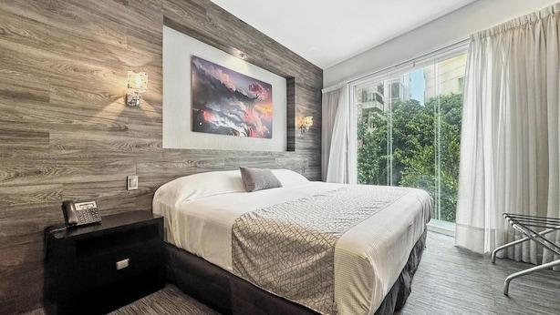 A modern bedroom with a large bed, a nightstand, a wall-mounted phone, and a window with curtains. - Elite 47 Unity (Huixquilucan)